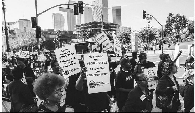 Black and white photo of Black workers marching the streets of LA holding signs that say "We want our WORKSITES to look like our COMMUNITIES"