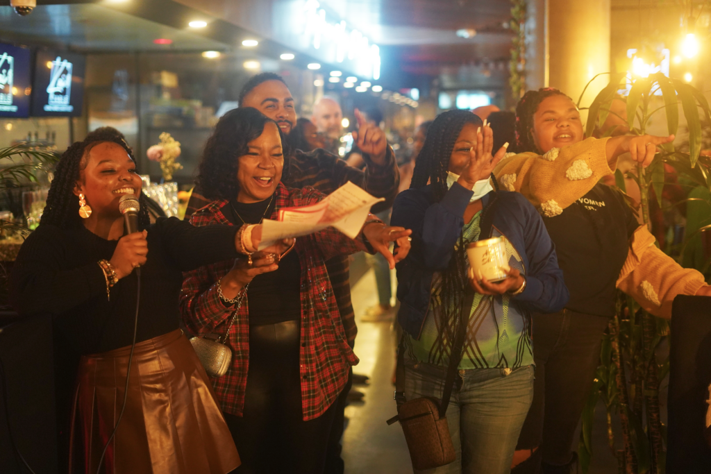 A group of Black women at a celebration point and laugh at something that is off-camera